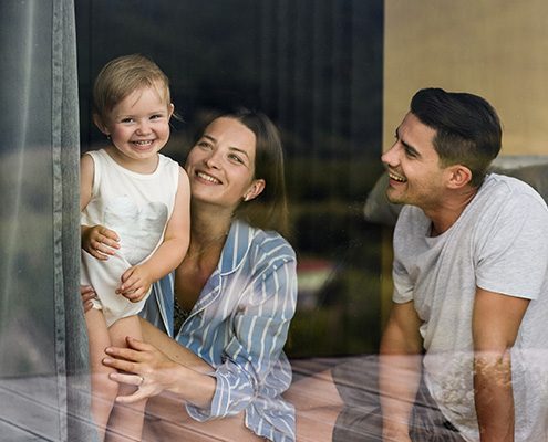 Junge Eltern mit ihrem Kind hinter einer Scheibe in ihrer Wohnung